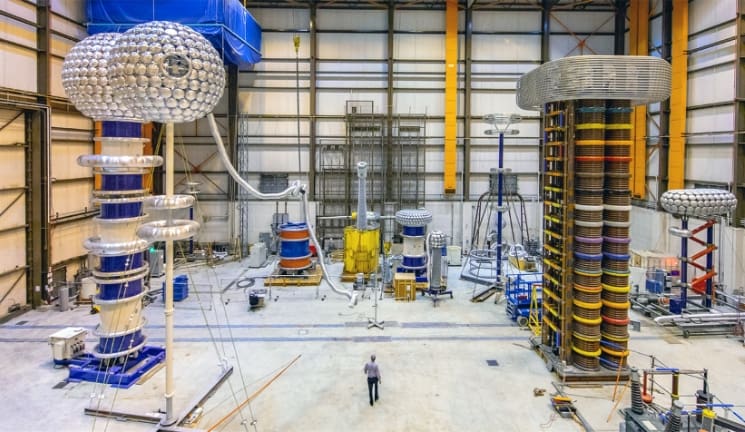 A view of the high voltage testing lab at Powertech. Multi-story Van de Graaf generators tower over the people in the lab.