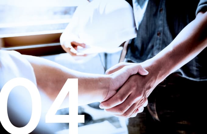 Close-up of two professionals shaking hands at a construction site, with one holding a safety helmet.