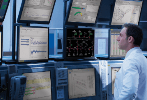 Engineer in a control room monitoring multiple data screens displaying real-time energy grid analytics and power system analysis software.
